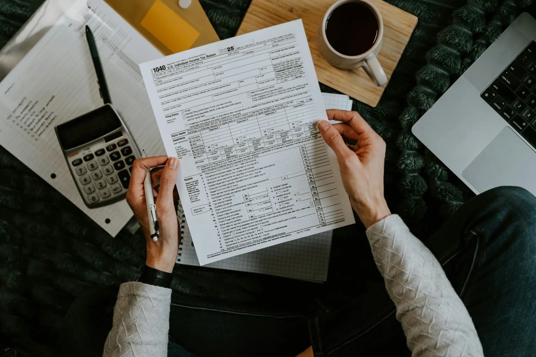 Hands with a calculator and printed tables beside a laptop